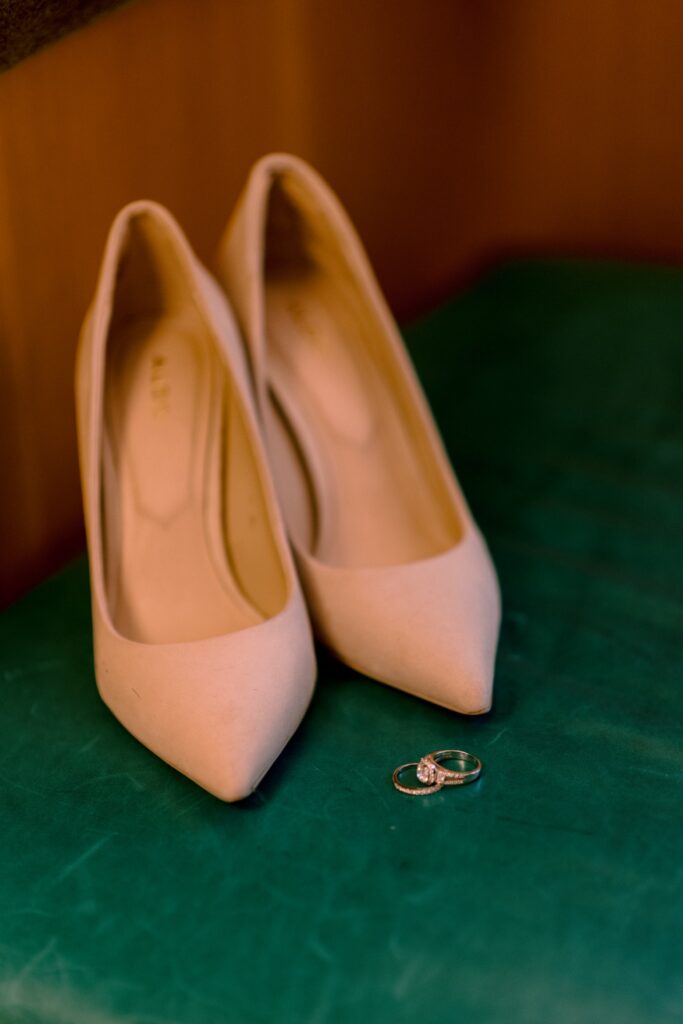 A pair of elegant ivory high heels with a diamond engagement ring placed between them on a green surface.