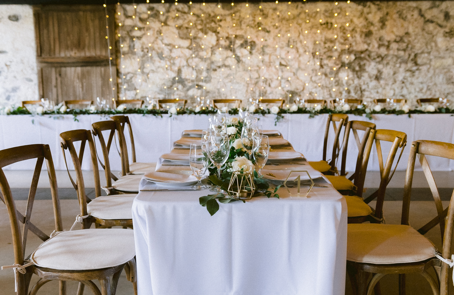 An elegantly set banquet table with floral centerpieces and string lights in a rustic venue
