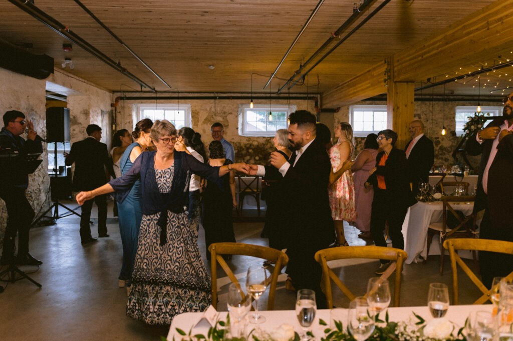 Guests hand in hand dance at the centre of dance floor at a wedding.