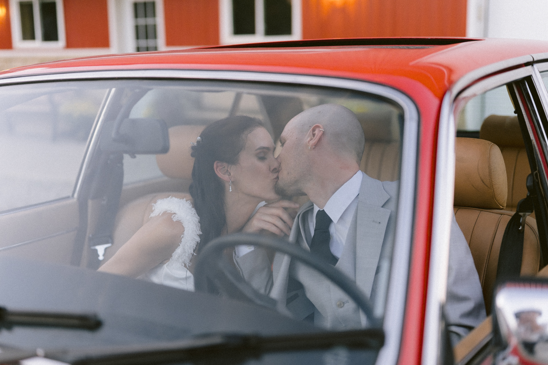 Newlyweds sharing a kiss inside a classic car.
