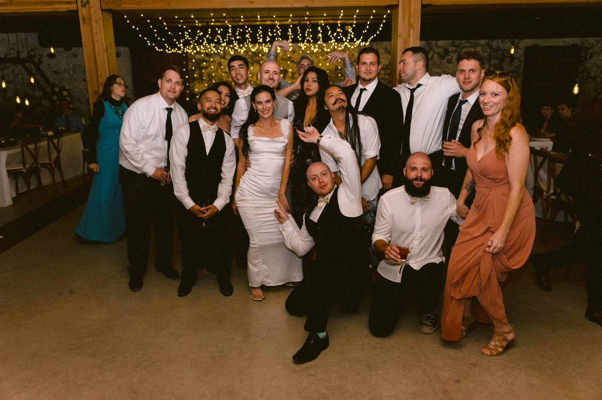 A group of people at a wedding posing for a photo, with some making playful gestures.