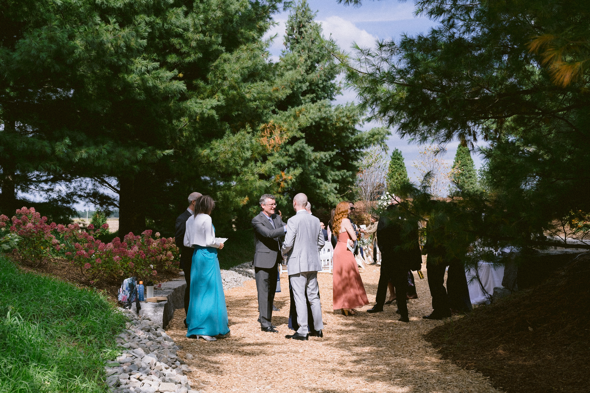 Guests gathered in a garden for a wedding, with trees and shrubs surrounding the area at Cambium Farms wedding.