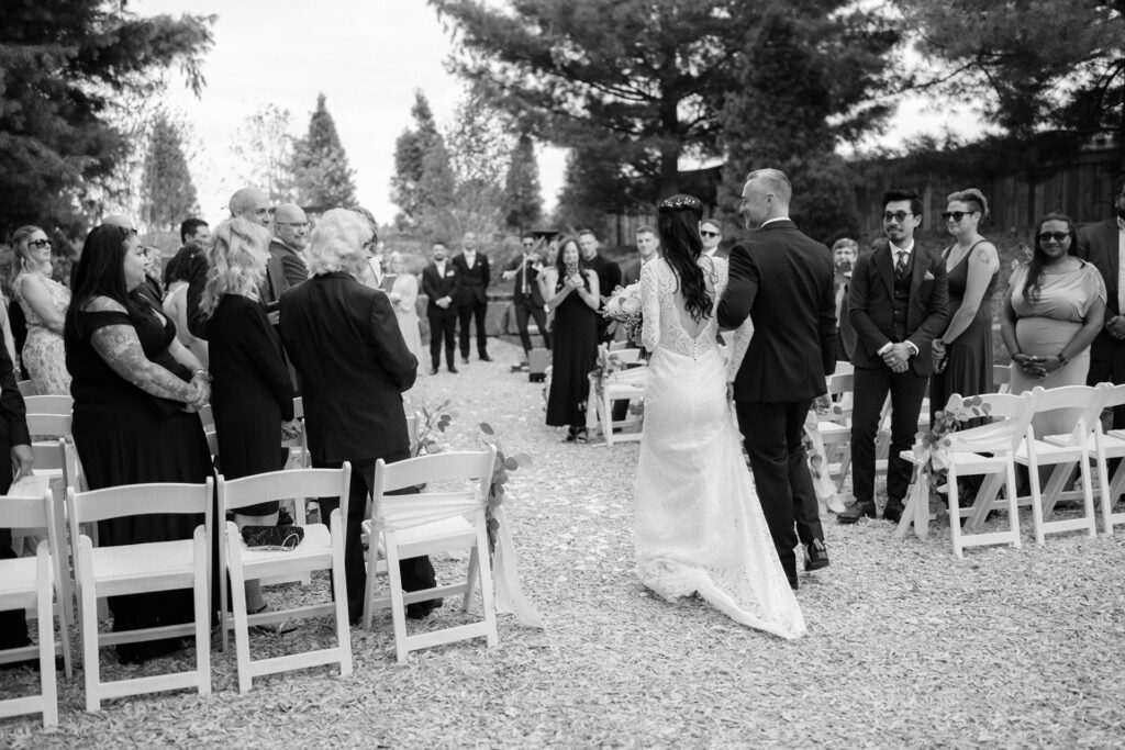 A bride walking down the aisle while guests watch at an outdoor wedding ceremony at Cambium Farms.