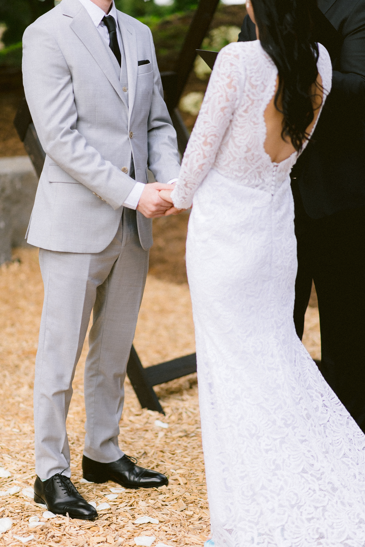 Bride and groom holding hands on their wedding day, with the focus on their interlocked hands and wedding attire.