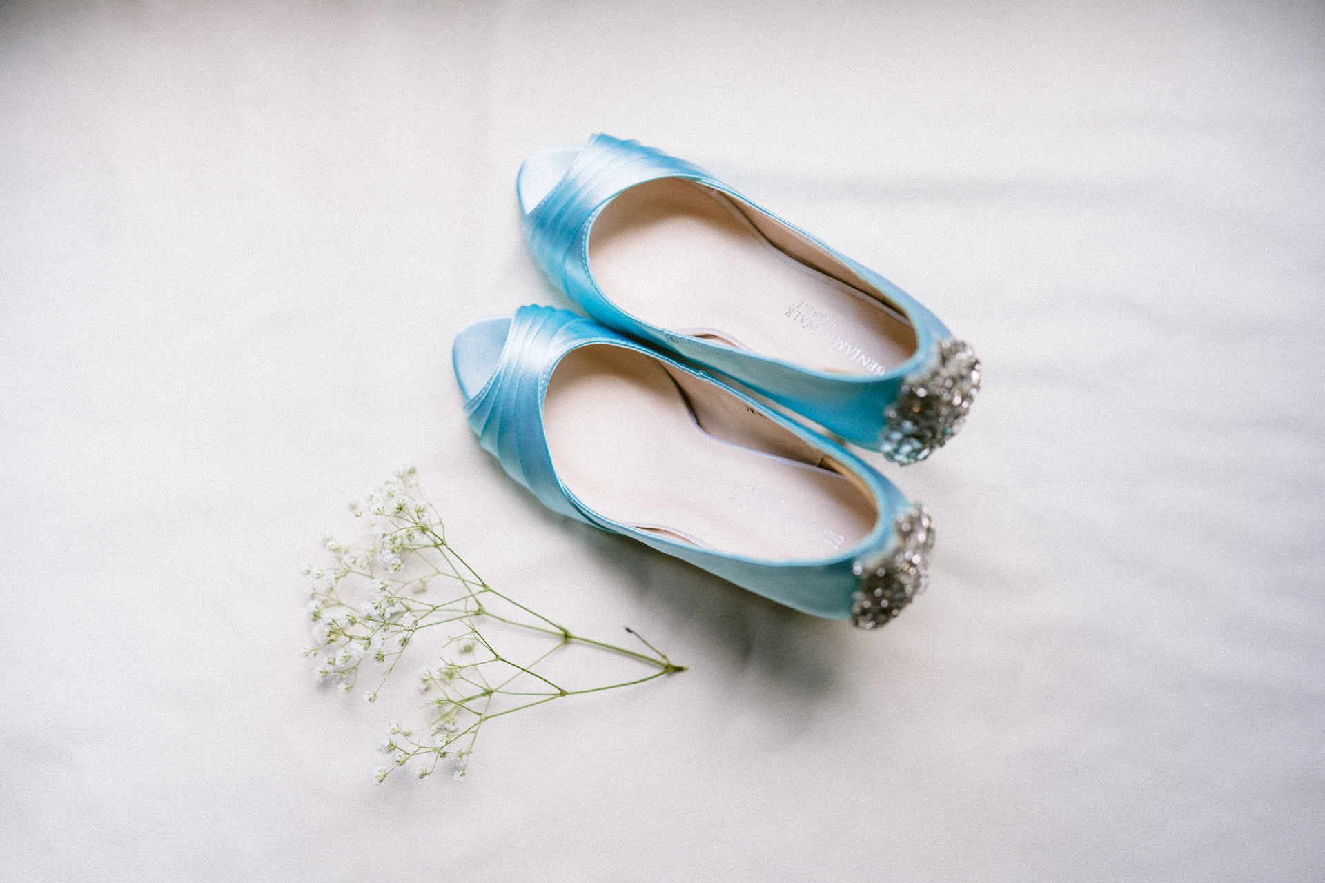 A pair of blue bridal shoes positioned next to delicate white flowers on a light background