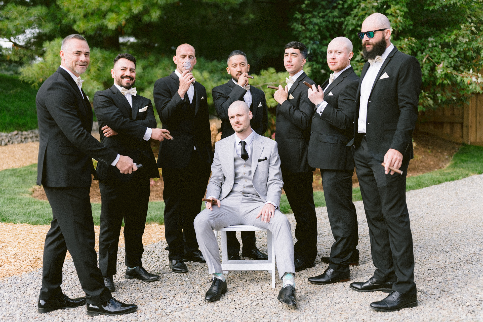 Group of men in suits posing with a seated groom in the center, making playful gestures