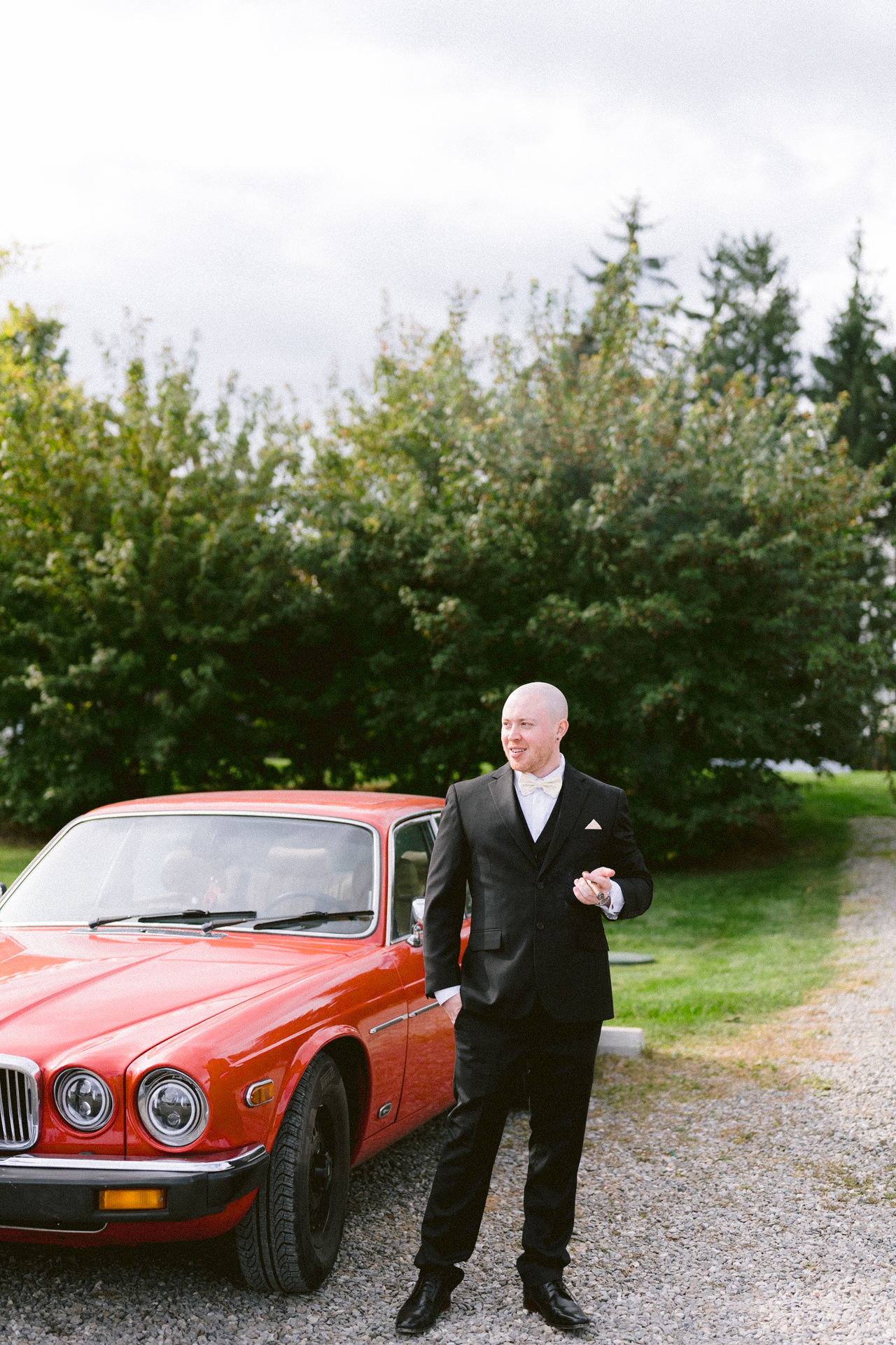 A man with a cigar posing besides a red vintage car.