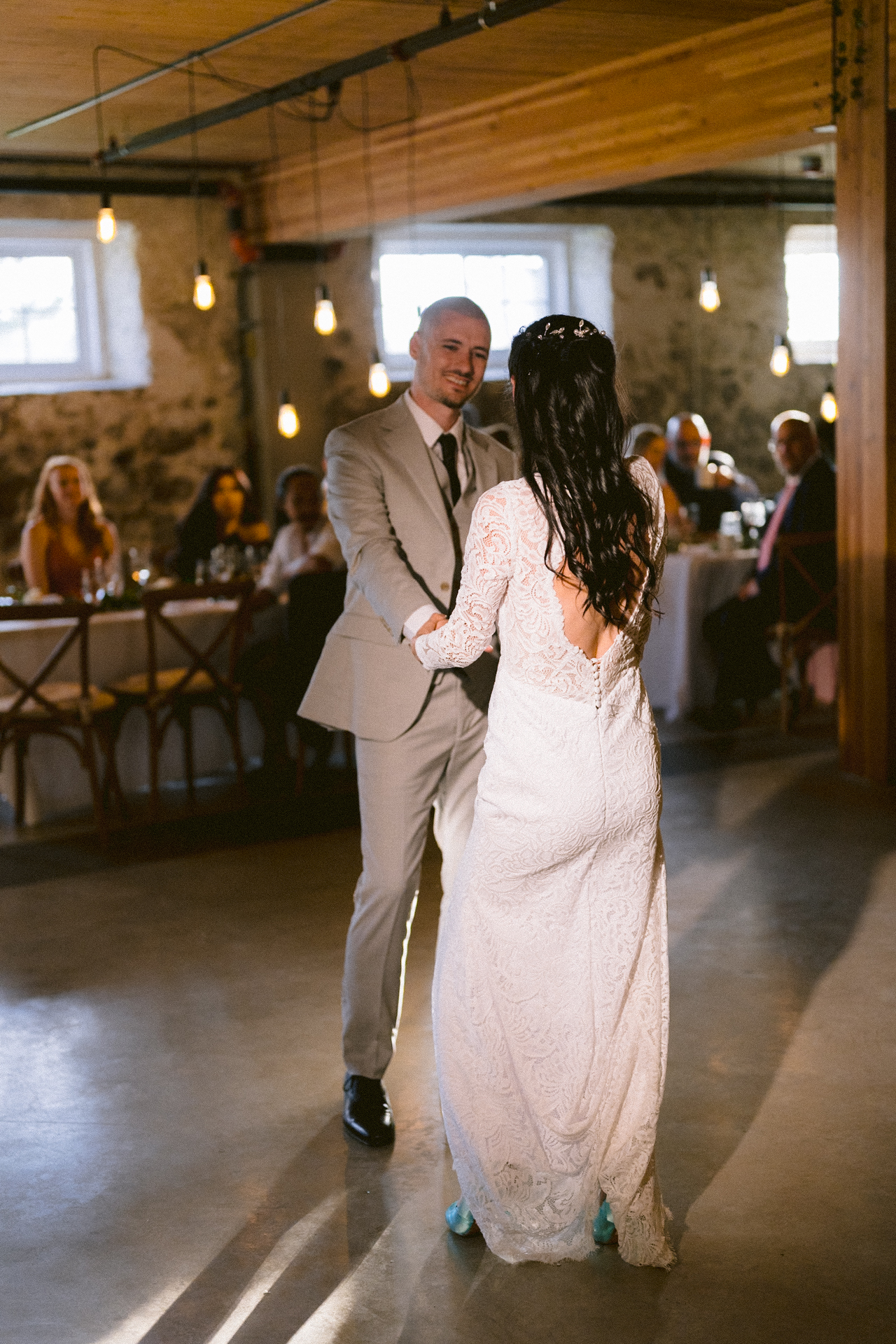 A couple sharing a dance in a warmly lit venue, with guests seated in the background