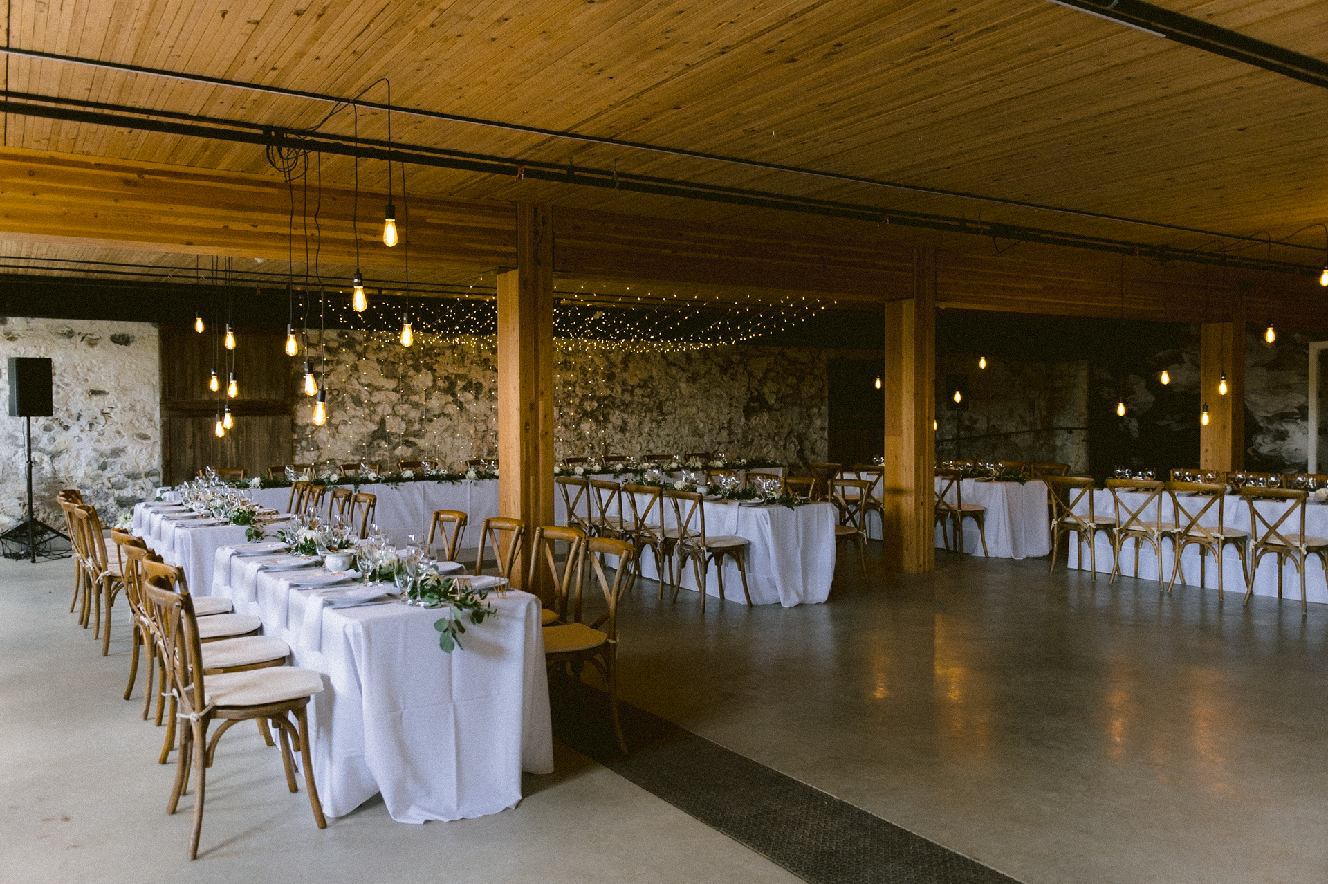A rustic backdrop with hanging lights and elegant flower displays, setting the stage for a romantic wedding at The Byre, Cambium Farms.