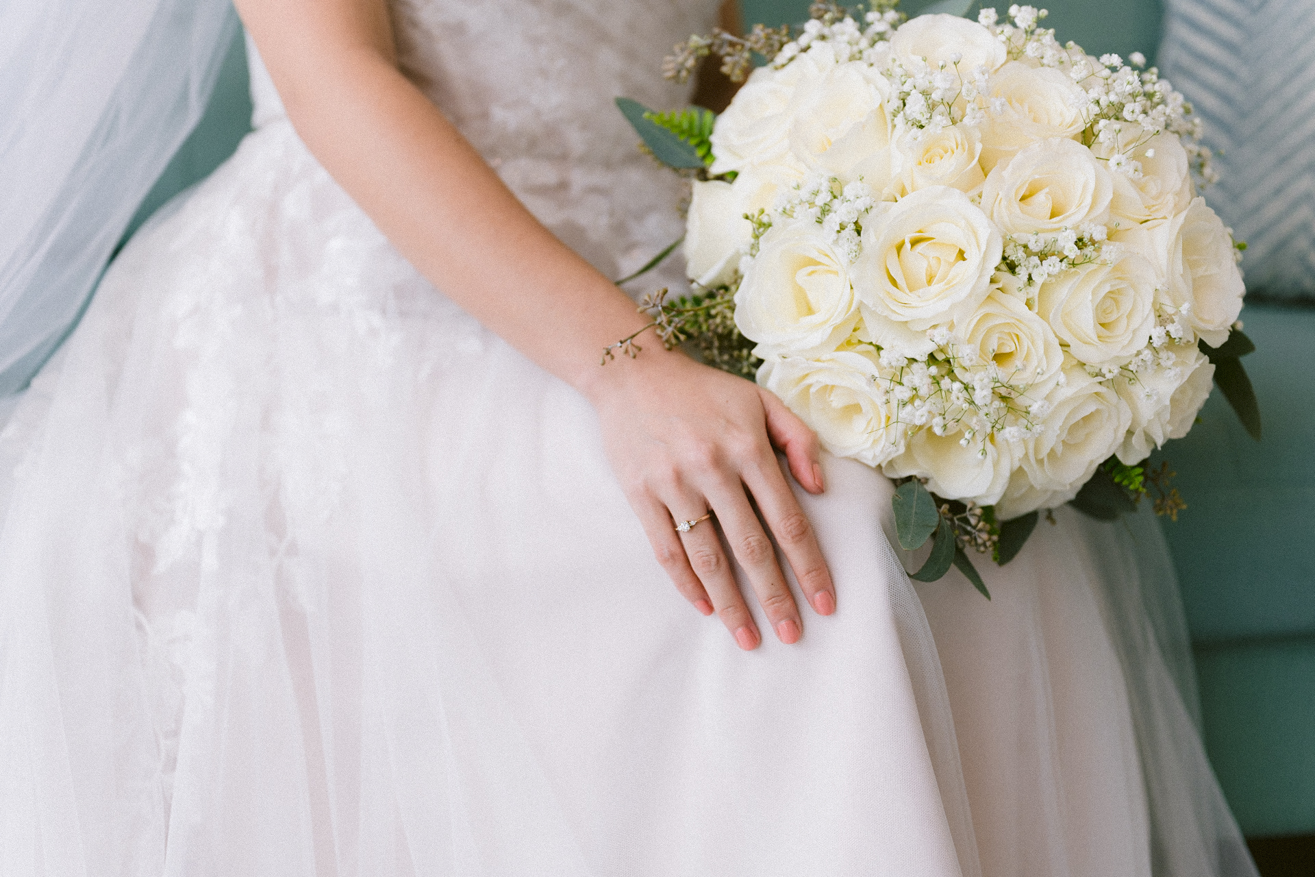 Bride holding a bouquet of white roses with a focus on her hand and wedding ring.