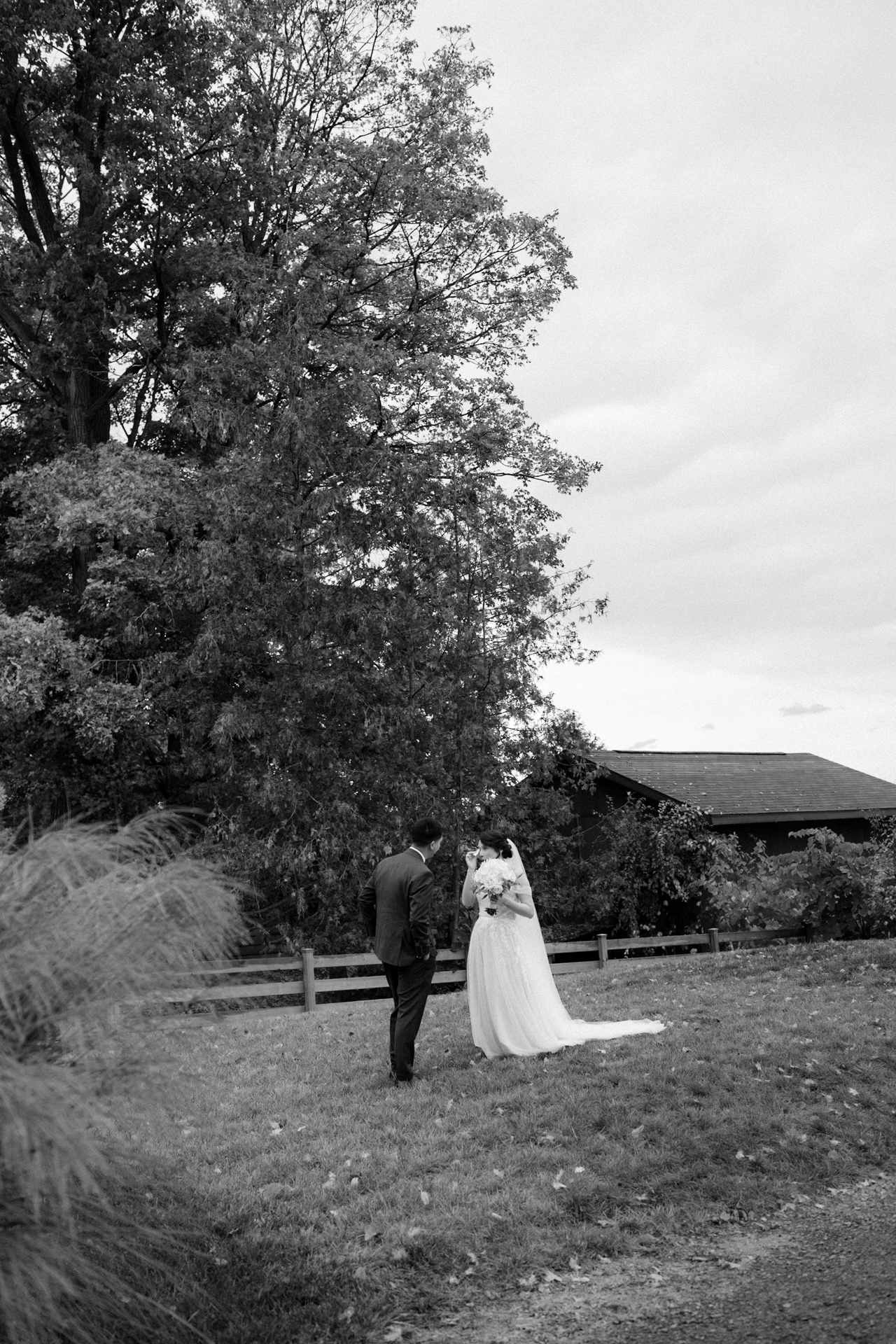 A bride and groom standing together on a lawn with autumn foliage in the background