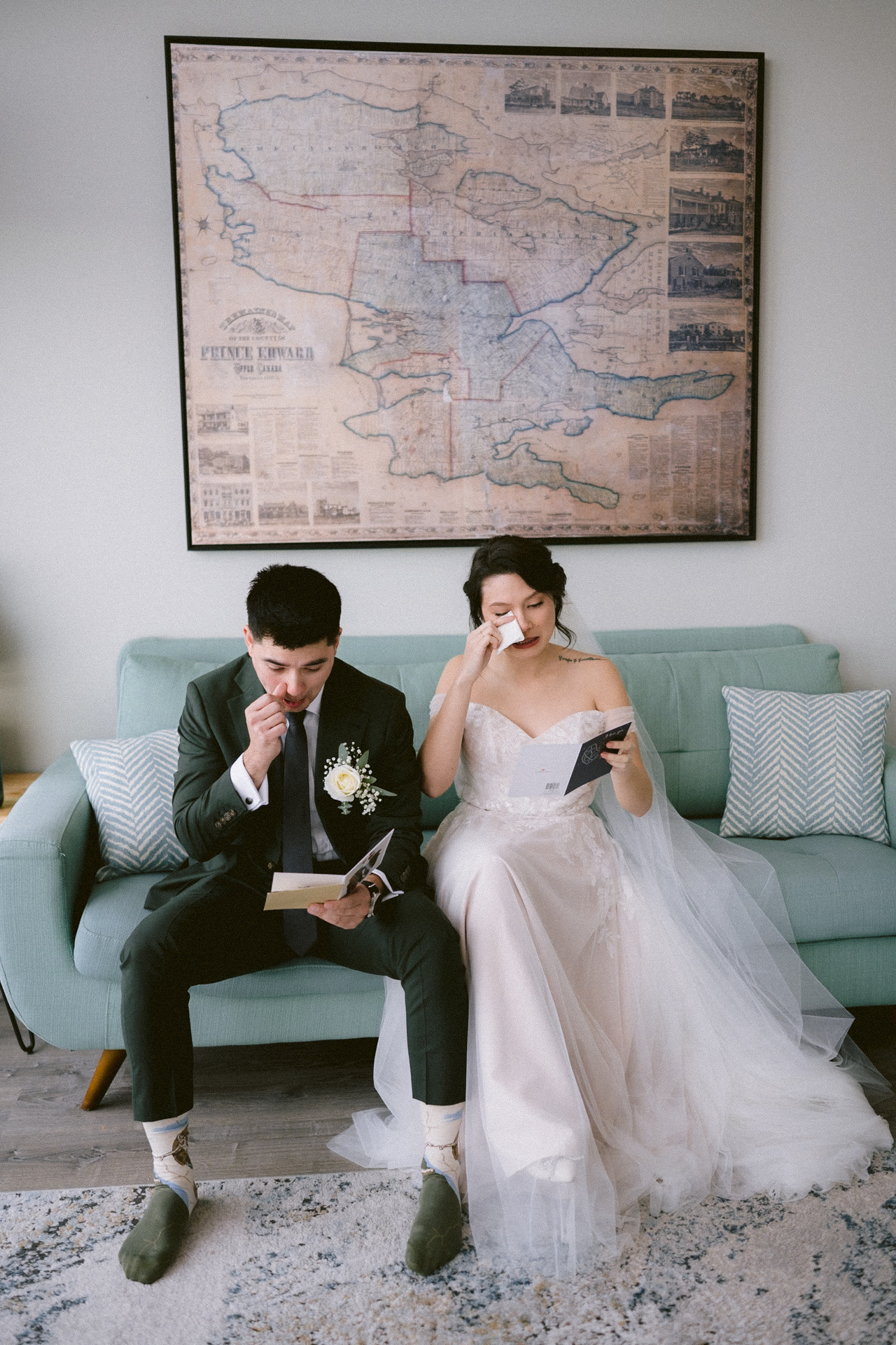 A bride and groom sitting on a sofa, reading heartfelt notes, with the groom appearing to wipe a tear and the bride smiling