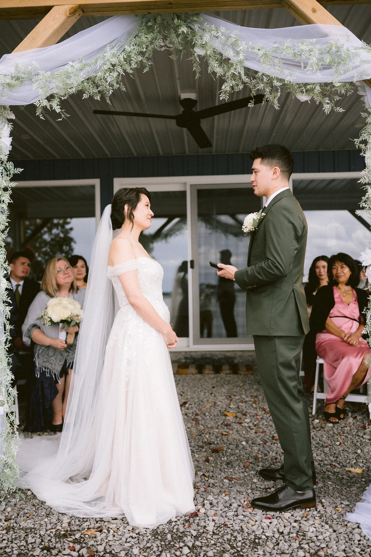 A couple exchanges vows at an outdoor wedding ceremony with guests looking on.