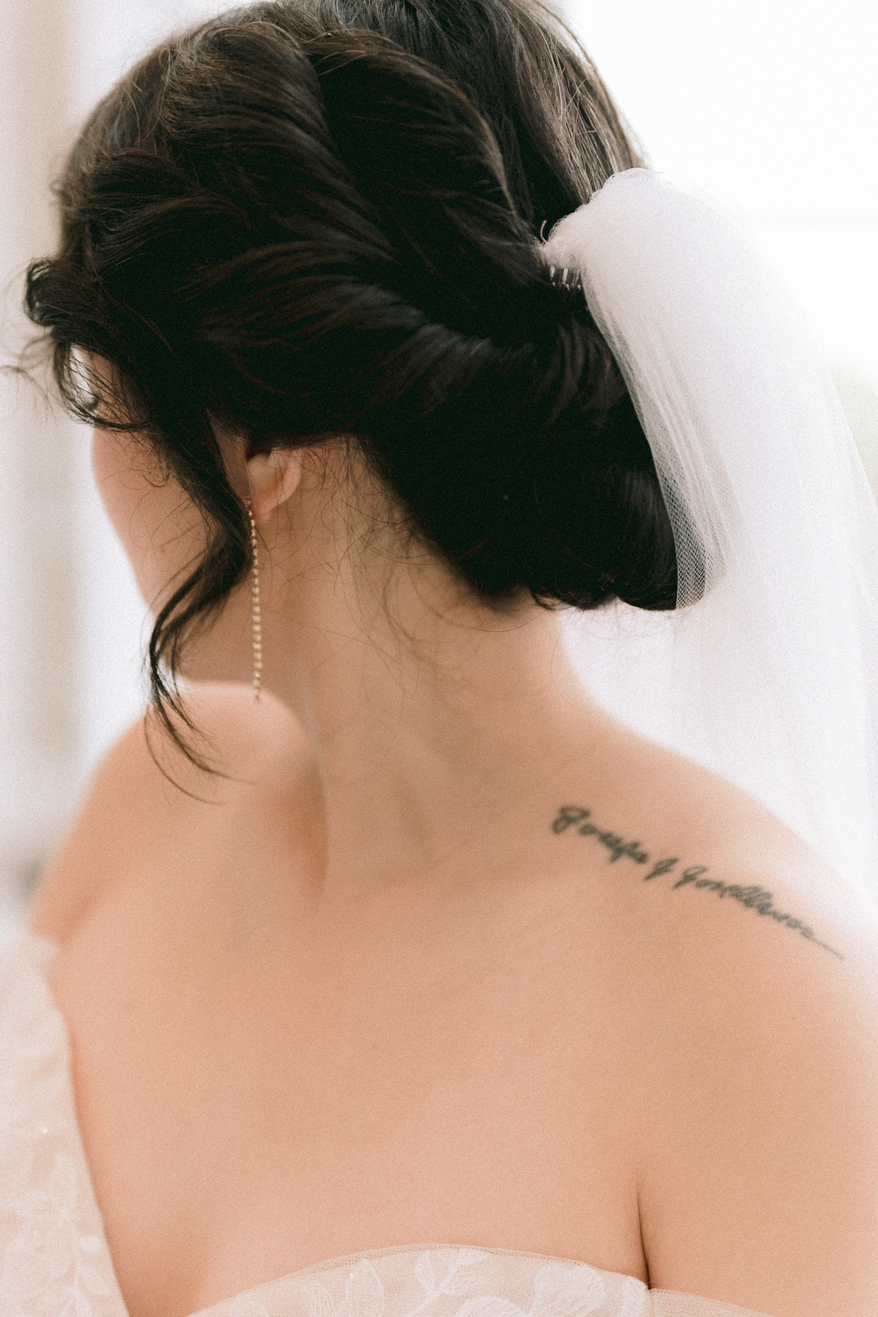 Bride with an elegant updo hairstyle and veil, showcasing a tattoo on her shoulder.