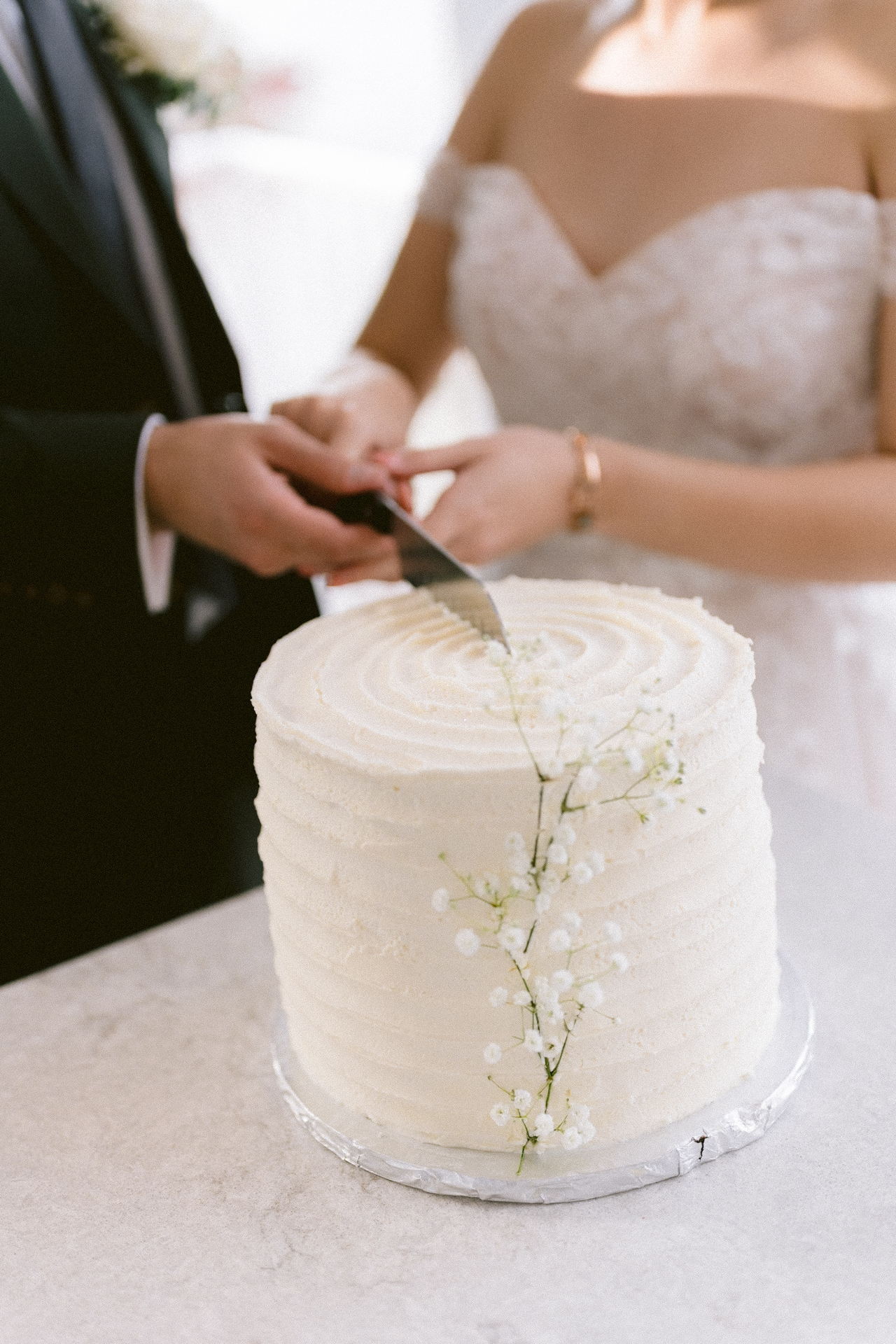 A bride and groom cutting a white wedding cake adorned with small flowers