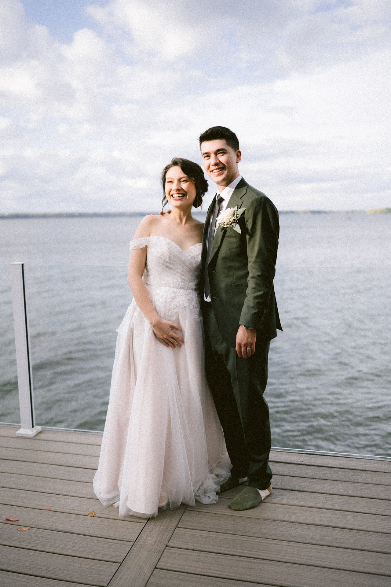 A bride and groom smiling together on a dock by the water