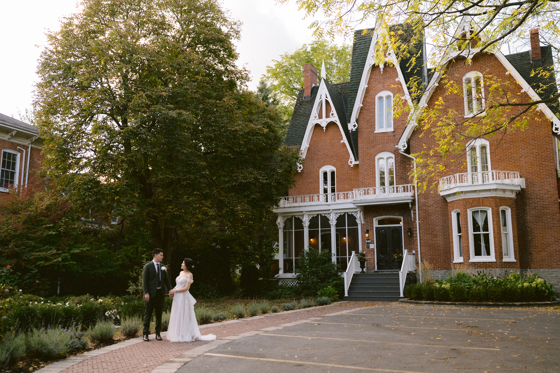A couple in wedding attire holding hands in front of a victorian-style house