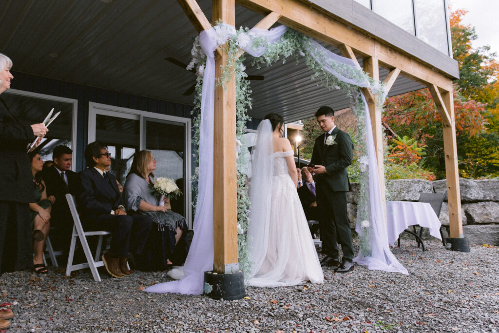 A couple exchanges vows at an outdoor wedding ceremony with guests looking on