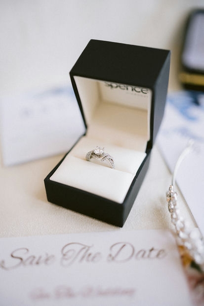 An engagement ring inside an open box placed on a table next to a 'save the date' invitation.