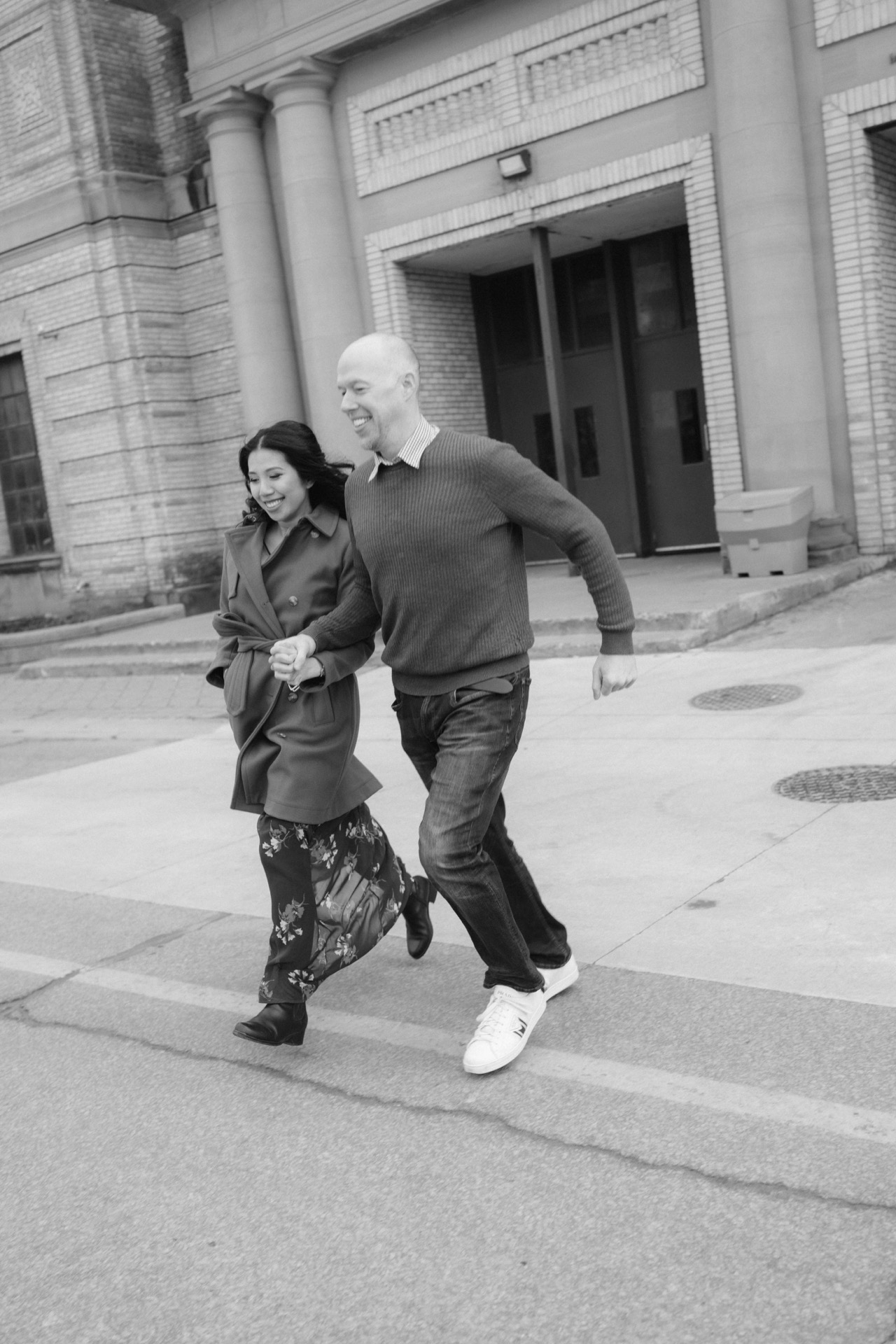 Two people walking briskly across a street in an urban setting, captured in black and white.