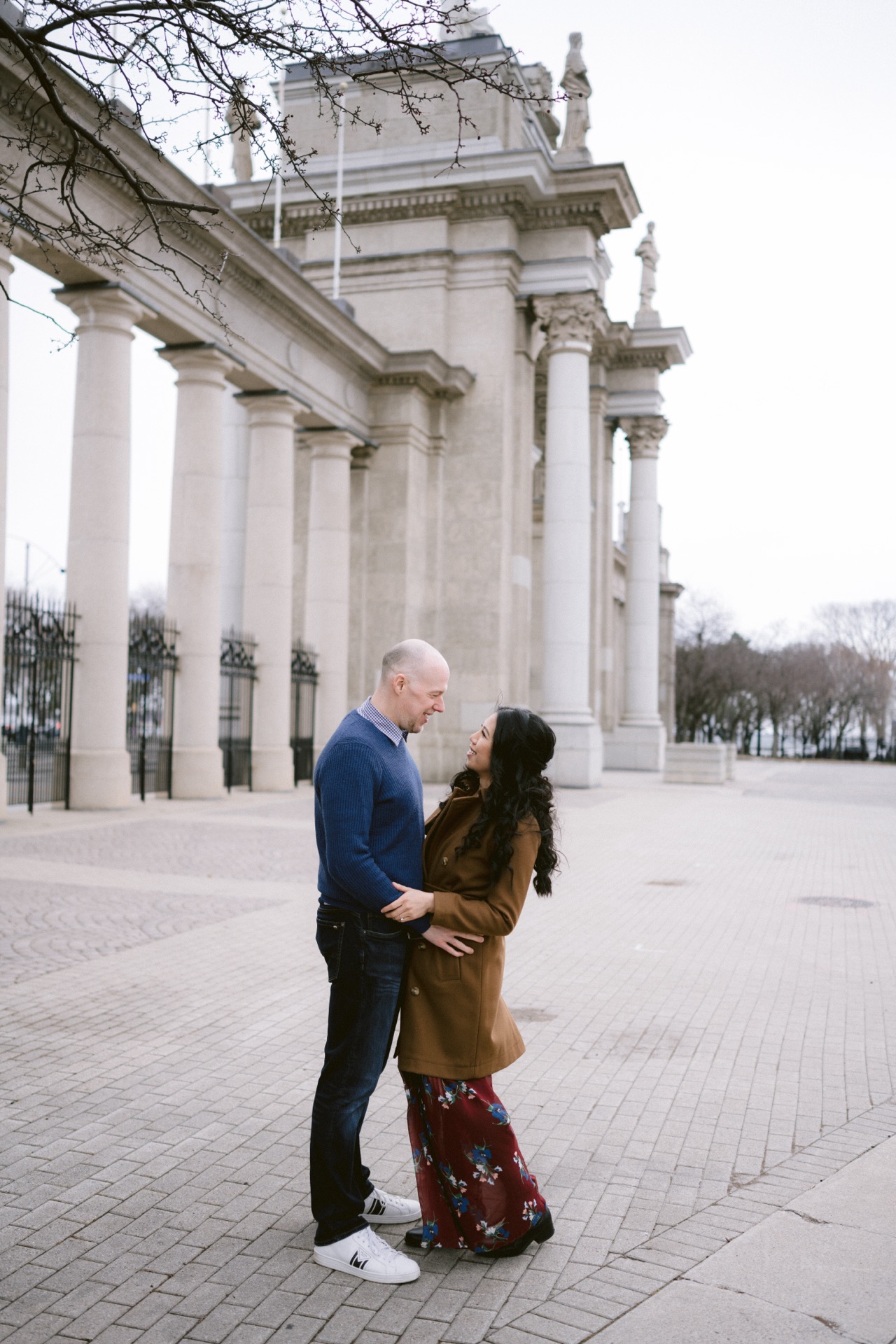 A couple standing close and looking at each other affectionately in front of a building with grand columns during their engagement session