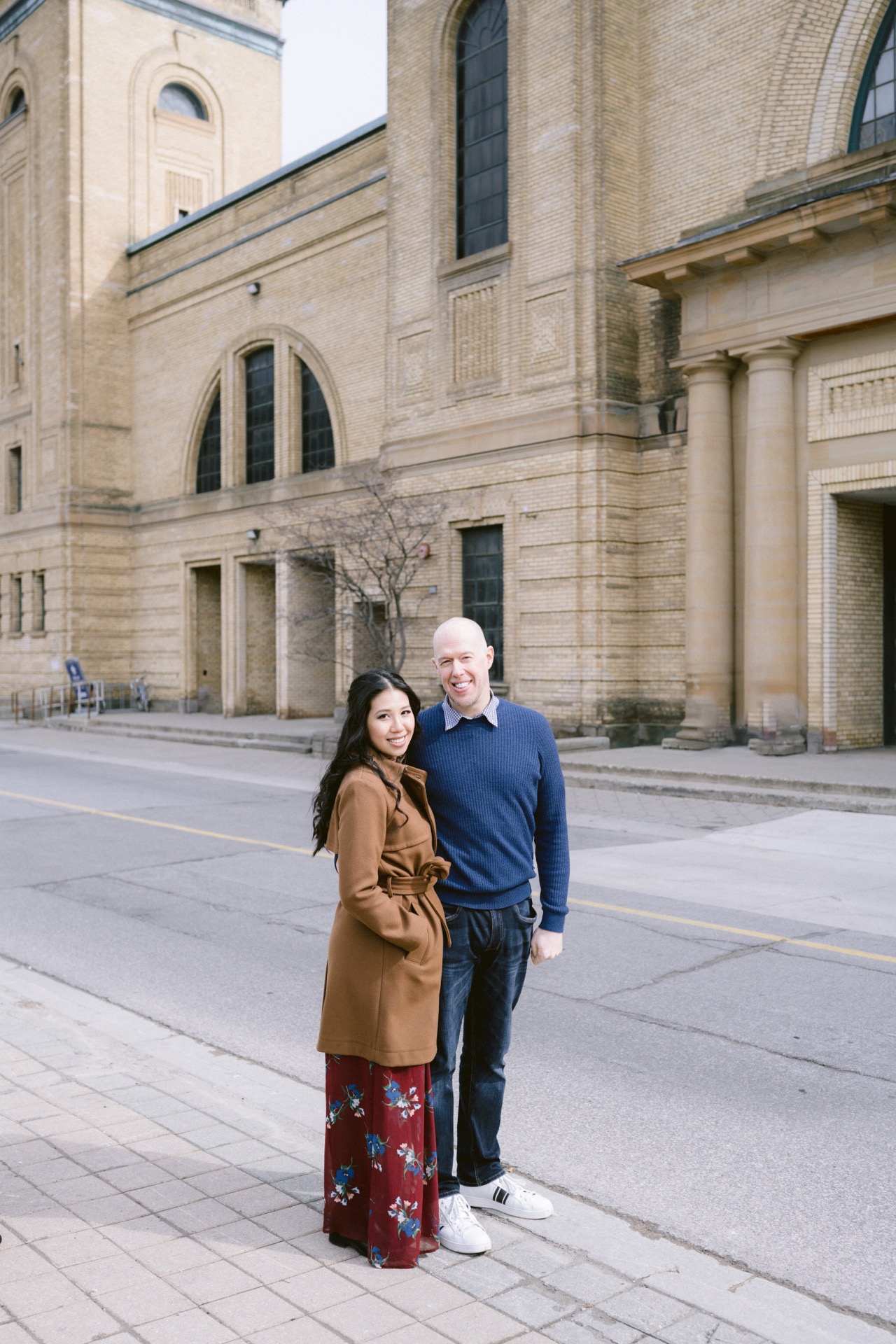 A couple standing together and smiling on a city street with Exhibition Place in the background