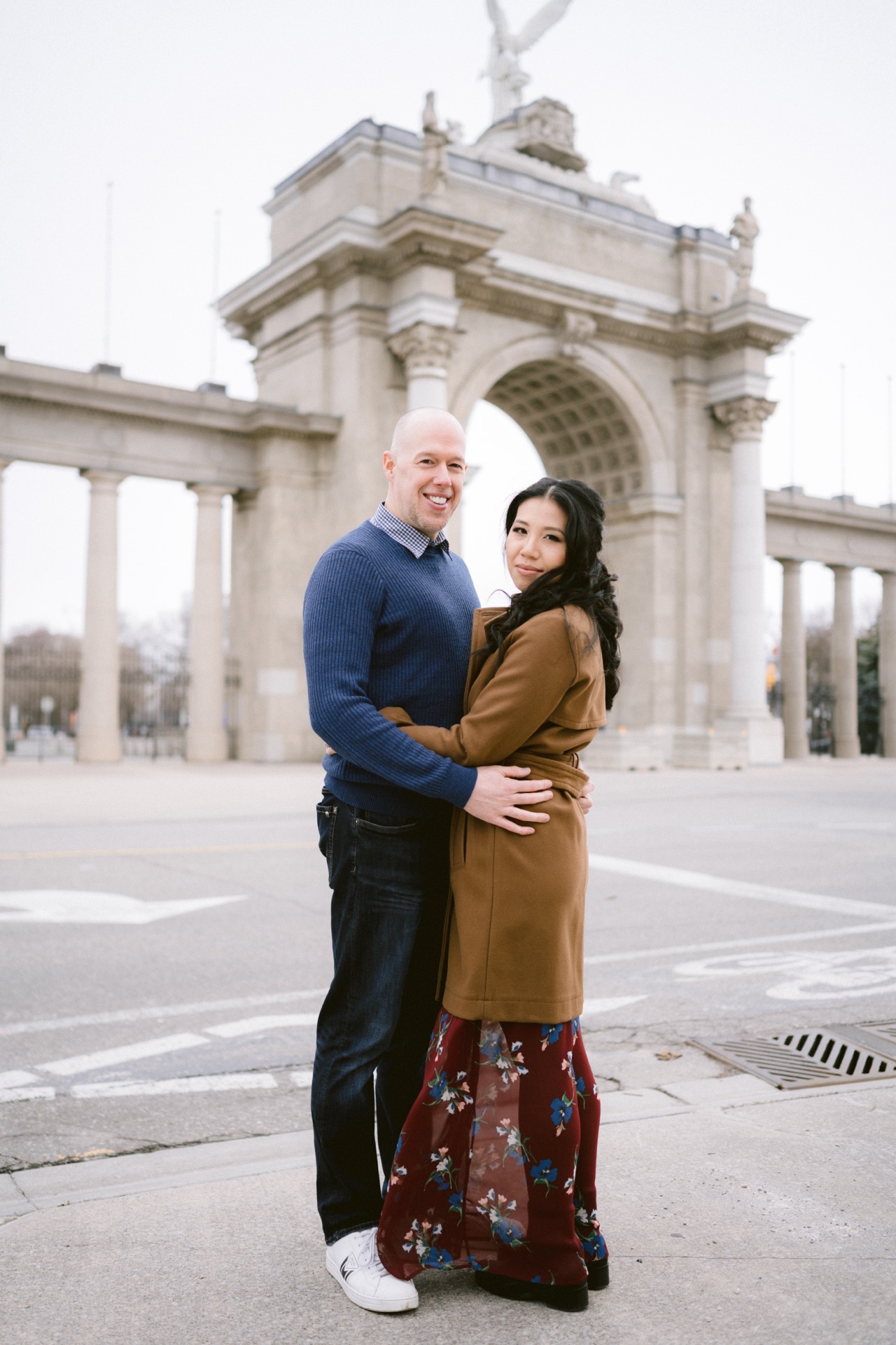 Couple embracing during their engagement session in front of an archway monument at Exhibition Place