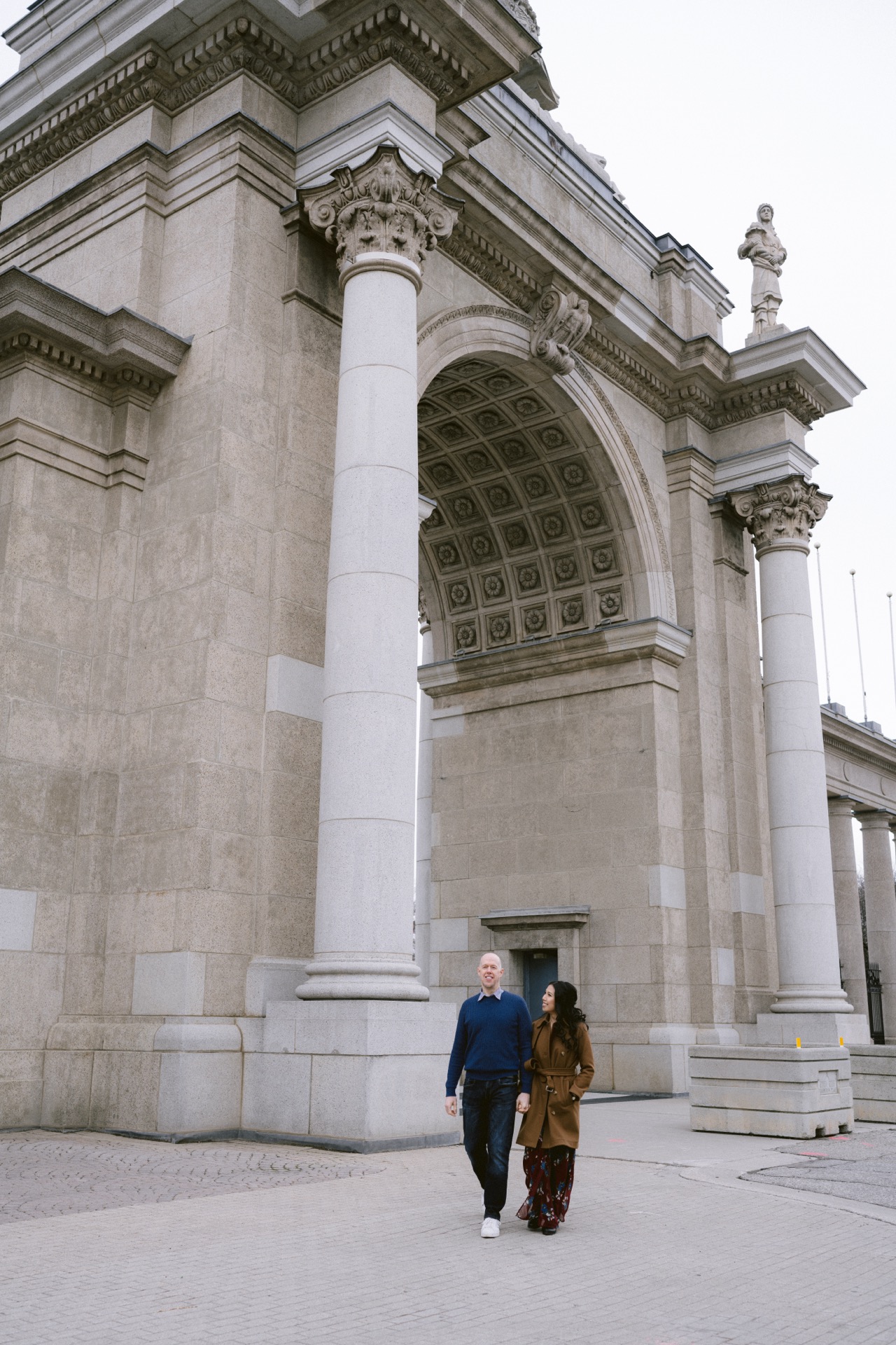 Two individuals walking by a grand neoclassical archway.