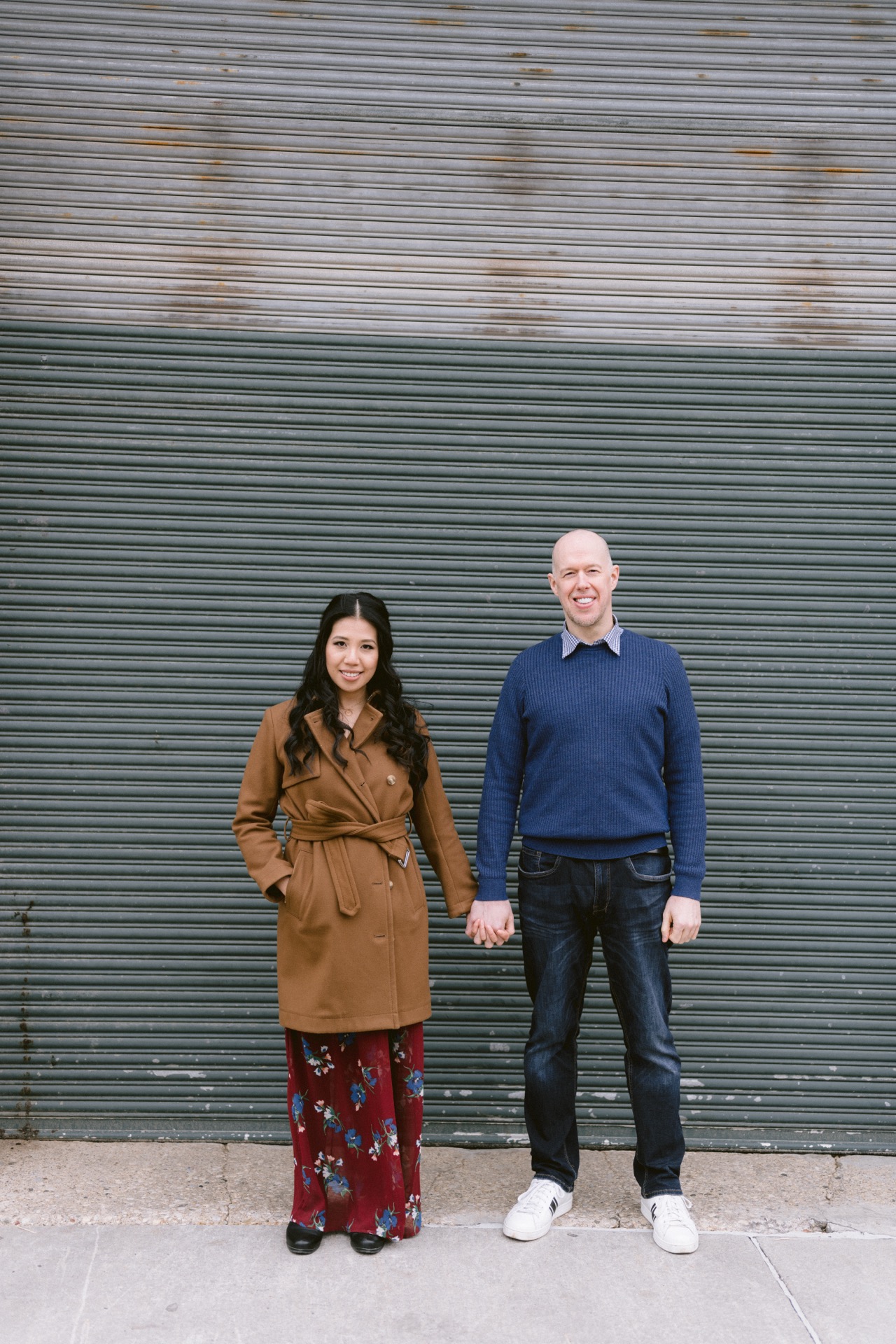 A man and a woman standing side by side in front of a corrugated metal wall.