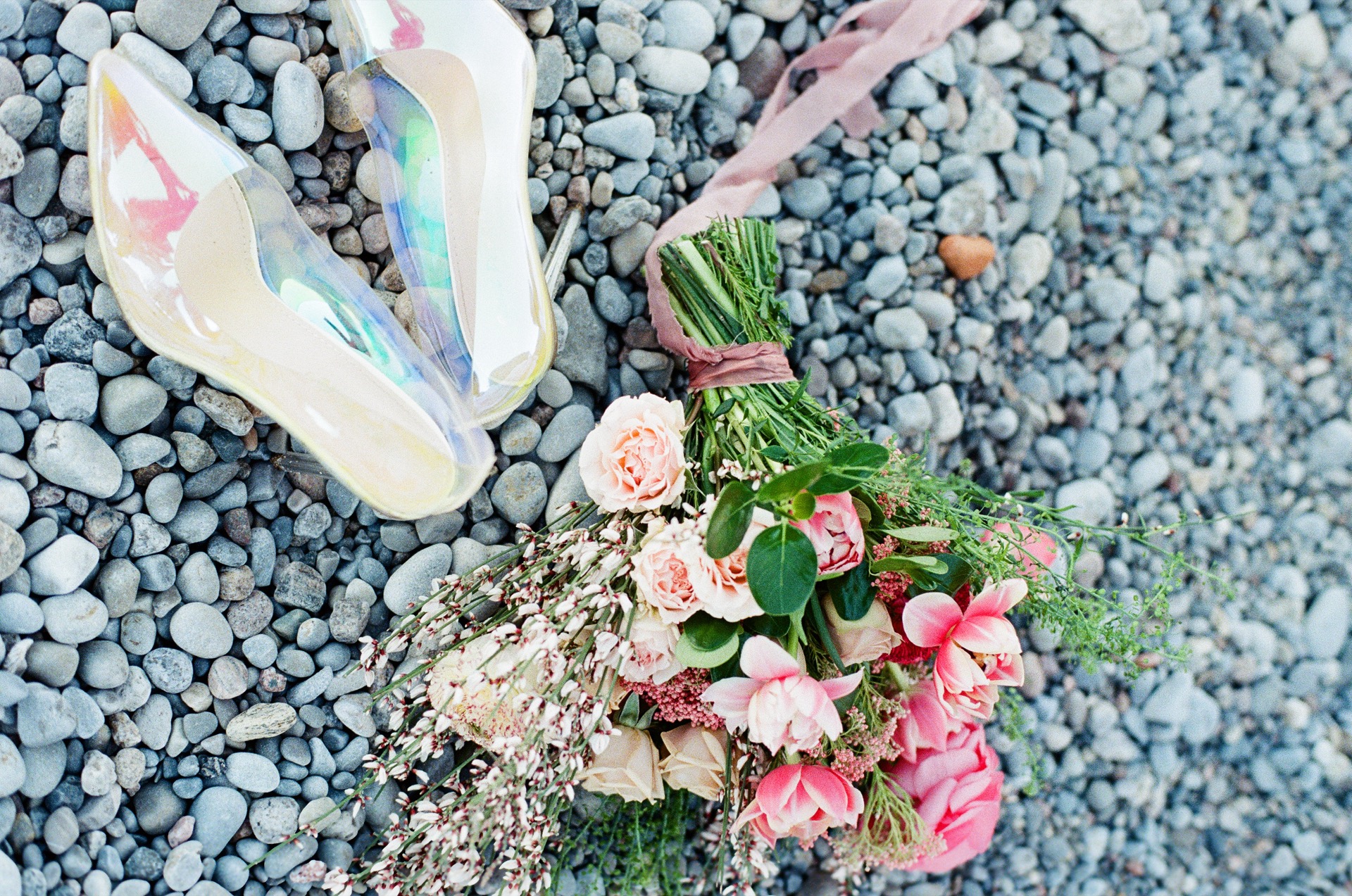 A pair of colourful wedding shoe displayed by the side of a wedding bouquet.
