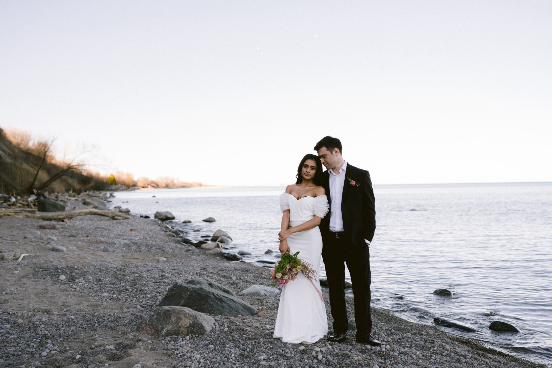 The newlywed poses for their couple portrait by Lake Ontario near Sunrise Hill.