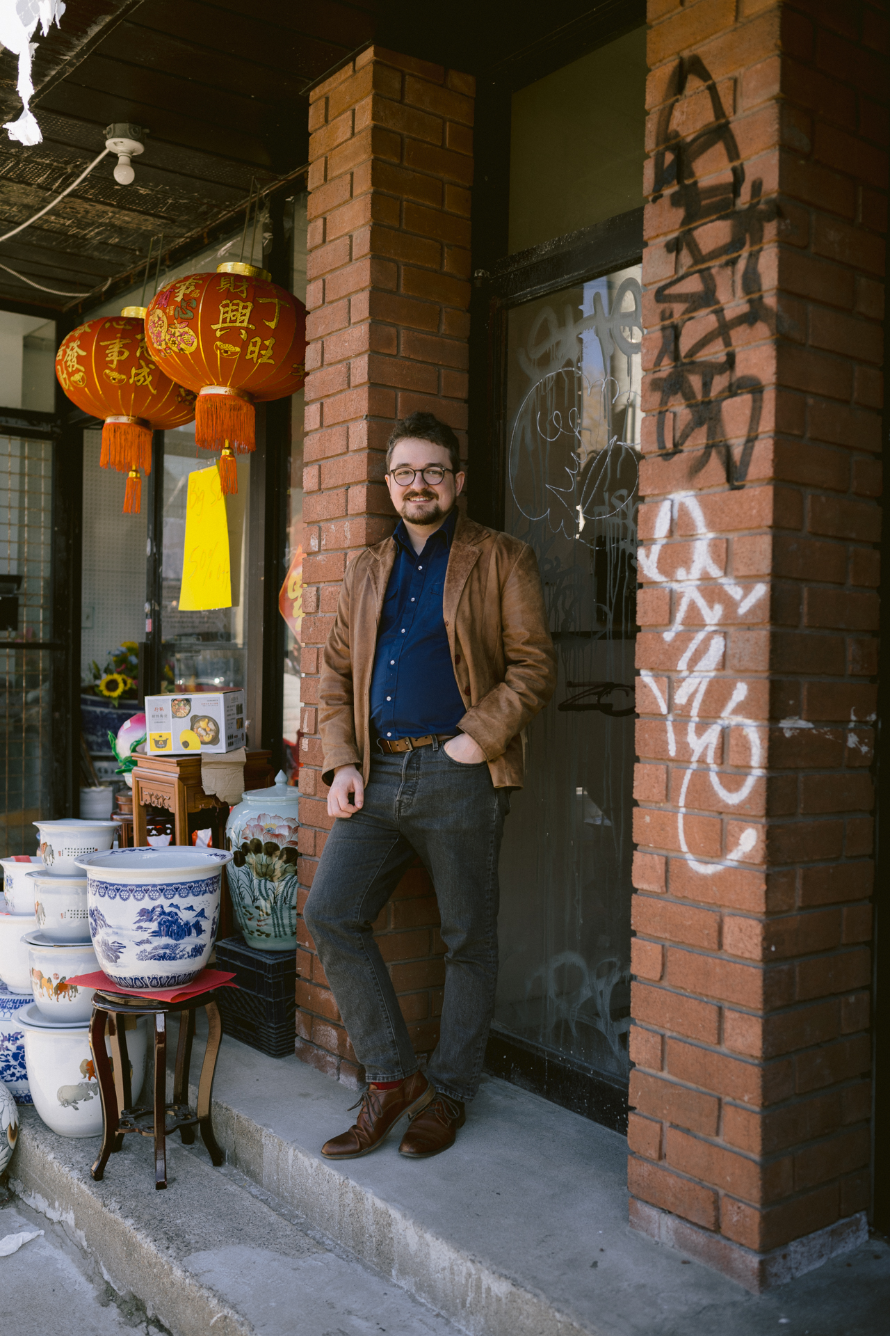 A man poses in front of a Chinese antique shop for his engagement session.