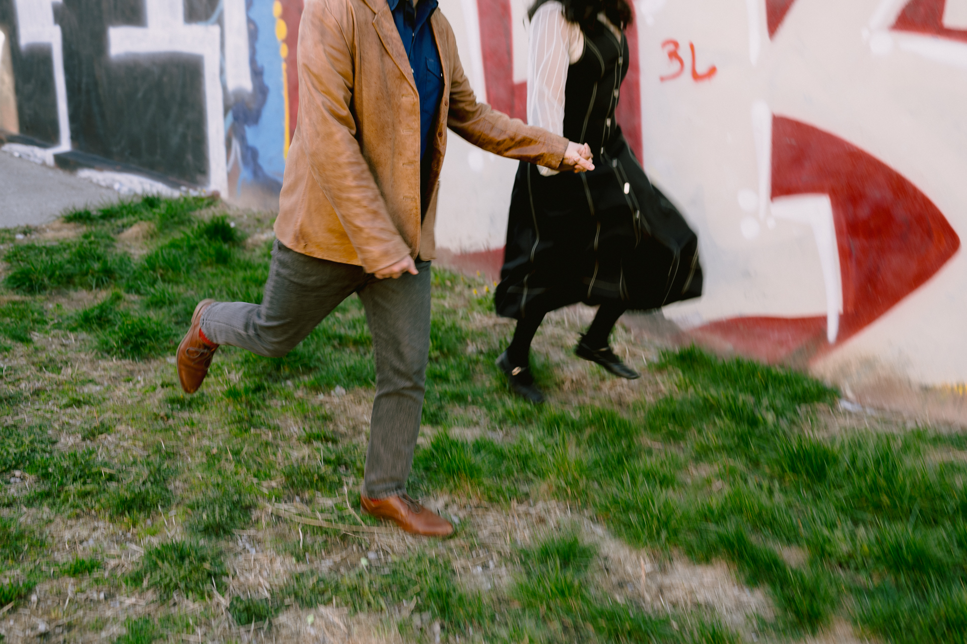 Couple run and play around in front of an artistic mural for engagement photographer Toronto to capture their candid moment.