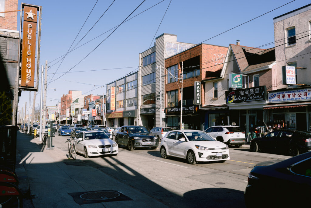 The street view of Gerrard Street with cars parking on both sides of shops.