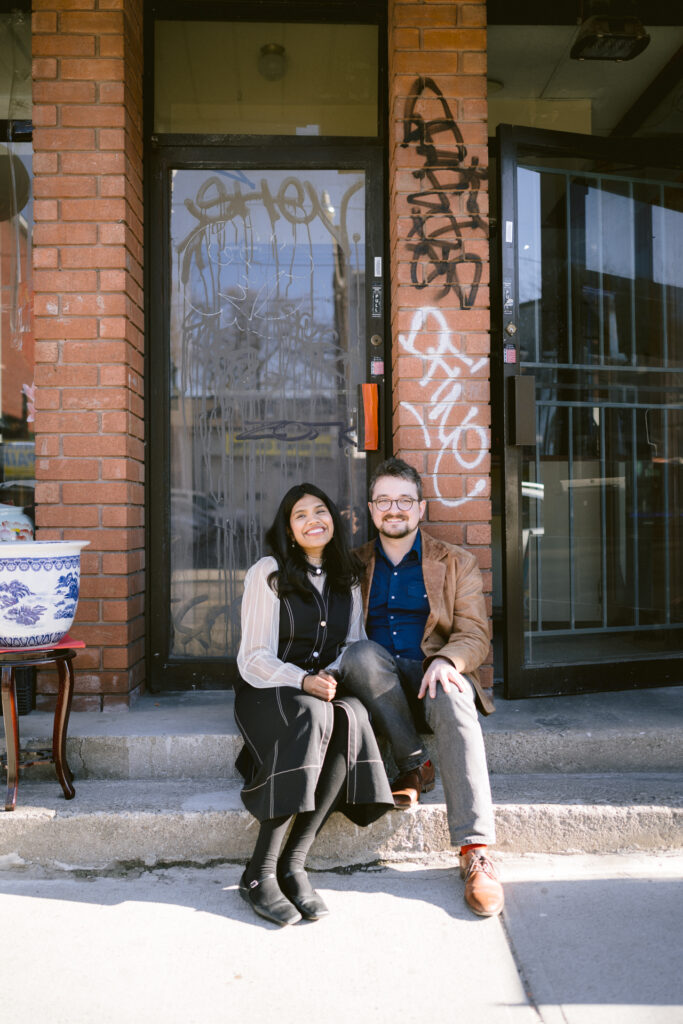 A couple sit in front of a pho restaurant at Gerrard Street with an engagement photographer Toronto.