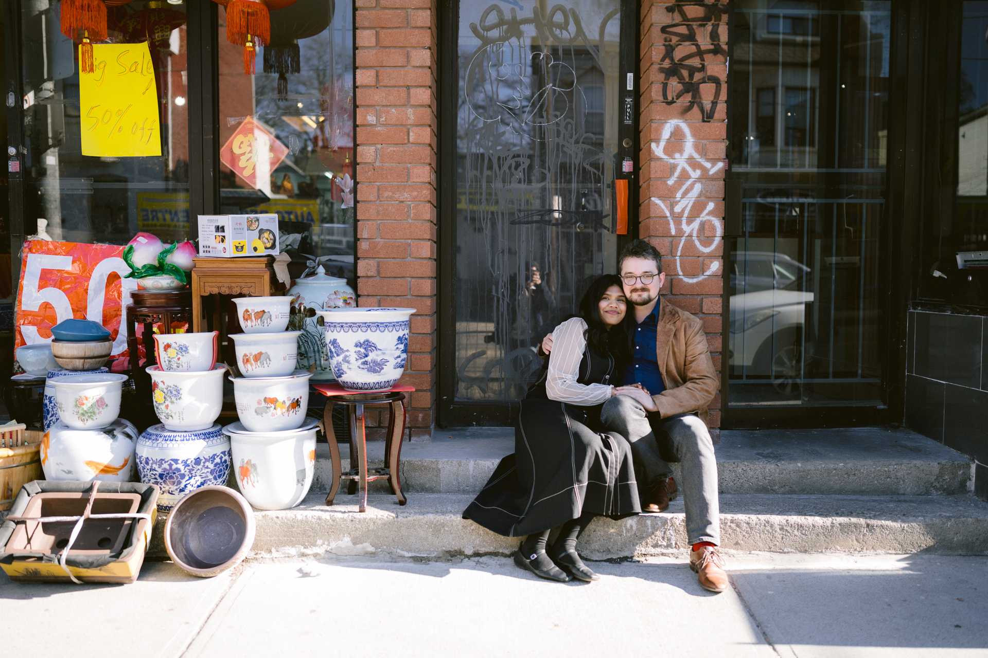 Couple holds hands and sit down together in front of Chinese antique shop during their photoshoot.